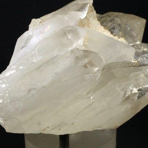 Puede incluir: Un grupo de cristales de cuarzo transparente. El cuarzo tiene una apariencia translúcida, con estructuras internas visibles y un tono ligeramente lechoso. Los cristales están dispuestos en una formación en capas, con bordes y puntas afiladas.