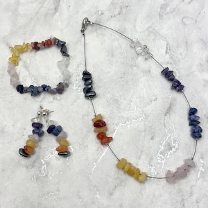 May include: A set of gemstone jewelry featuring a necklace, bracelet, and earrings. The necklace and bracelet are made with a variety of colorful stones, including yellow, orange, red, purple, blue, and white. The earrings are a matching pair of dangle earrings with the same stones.