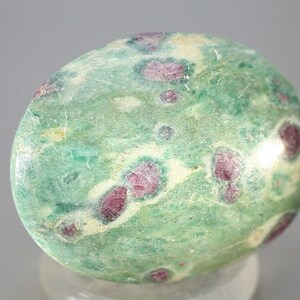 May include: A green and pink gemstone with a smooth, polished surface. The stone has a swirling pattern of green and white, with small pink inclusions throughout.