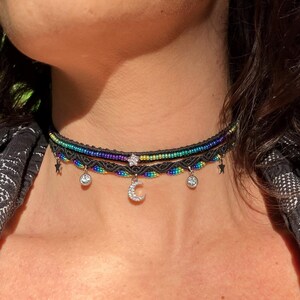 May include: A black choker necklace with three layers of colorful beaded string and silver star and crescent moon charms.