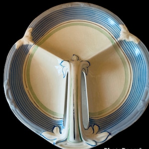 Op de afbeelding: Een witte keramische serveerschaal met drie secties. De schaal heeft een blauwe en groene gestreepte rand en een decoratief handvat in het midden.