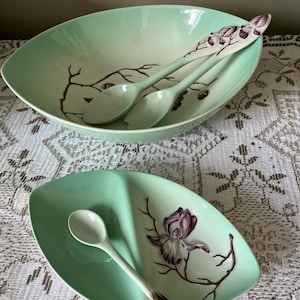 May include: A light green serving set comprising an oval bowl and a divided dish, both with a floral design of purple flowers and brown stems. The set includes three spoons with matching floral accents. The set is designed for serving.
