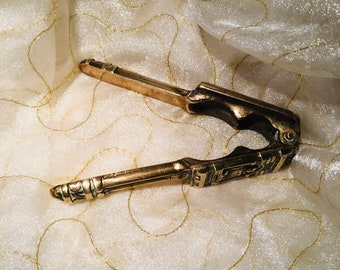May include: A brass nutcracker with an ornate design. The nutcracker is open and ready to crack nuts.