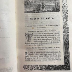 May include: An open book displaying French text and illustrations. The page is titled "PRIÈRES DU MATIN" and includes an engraving of figures kneeling before a cross. Decorative borders and religious symbols are also visible.