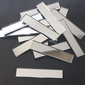 Puede incluir: Un montón de azulejos de espejo rectangulares plateados. Los azulejos miden aproximadamente 5 cm por 15 cm.