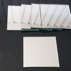 May include: A set of six small, square, silver-backed mirrors. The mirrors are arranged in a row, with the bottom mirror slightly offset from the others. The mirrors are on a black surface.
