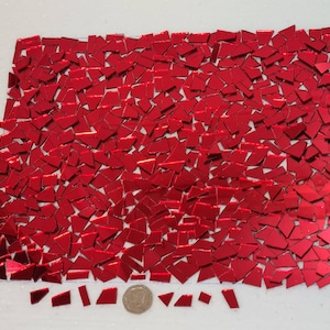 May include: A sheet of red, iridescent, mosaic tiles. The tiles are various shapes and sizes, and are arranged in a random pattern. There are a few extra tiles scattered below the sheet.