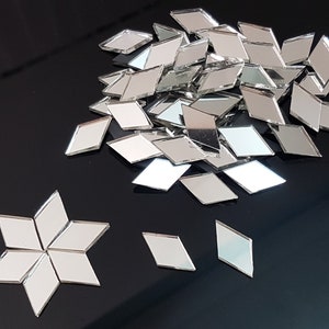 May include: A pile of silver diamond-shaped mirror tiles, with a few tiles arranged in a star shape.