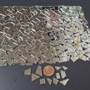 Może przedstawiać: Zbiór małych, nieregularnych płytek lustrzanych o różnych geometrycznych kształtach. Odbijające powierzchnie srebrnych płytek tworzą efekt mozaiki. Moneta jest dołączona jako odniesienie do rozmiaru.