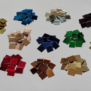 Könnte beinhalten: Sortiment von 12 kleinen quadratischen Spiegelkacheln in verschiedenen Farben, darunter Gold, Silber, Rot, Blau, Grün und Lila. Die Kacheln sind in Reihen auf einer weißen Oberfläche angeordnet.