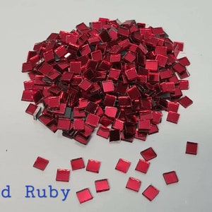 Könnte beinhalten: Ein Haufen kleiner, quadratischer, rot-rubinroter Spiegelkacheln. Die Kacheln sind auf einer weißen Oberfläche verstreut. Der Text "Red Ruby" ist in blauen Buchstaben unter dem Kachelhaufen geschrieben.
