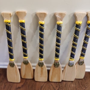 May include: Six wooden paddles with black and yellow striped handles. The paddles have a rounded top and a flat blade.