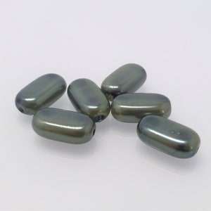 Könnte beinhalten: Sieben dunkelgraue, oval geformte Perlen mit glänzendem Finish liegen auf einer weißen Oberfläche. Jede Perle hat ein Loch in der Mitte, was darauf hindeutet, dass sie zum Auffädeln für Schmuck oder andere Bastelarbeiten gedacht sind.