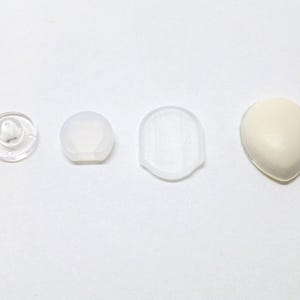 Op de afbeelding: Vier verschillende maten doorzichtige plastic oordopjes en een witte oordop.