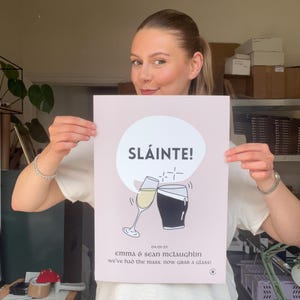 Op de afbeelding: Een roze poster met het woord "SL&Aacute;INTE!" in een witte cirkel, met illustraties van een champagneglas en een pint stout die klinken. De poster bevat de datum 04-01-25 en de namen Emma & Sean McLaughlin.