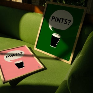 Puede incluir: Dos l&aacute;minas enmarcadas con marcos de madera. Una l&aacute;mina tiene fondo rosa, la otra es verde. Ambas presentan un gr&aacute;fico de pinta de cerveza negra y el texto "PINTS?" en un bocadillo. Las l&aacute;minas est&aacute;n sobre un sof&aacute; verde.