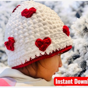 May include: A white crocheted hat with red heart appliqués. The hat has a red trim and is shown in a winter setting. The words "Instant Download" are in a red box in the lower right corner.