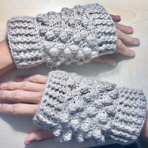 Puede incluir: Un par de guantes sin dedos de ganchillo beige con un diseño texturizado y abultado.