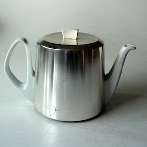 May include: A white ceramic teapot with a silver lid and a silver body. The teapot has a spout and a handle.