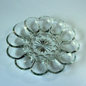 Könnte beinhalten: Eine klare Glasschüssel für Eier mit einem gewellten Rand und einem Diamantenmuster in der Mitte. Die Schüssel hat acht einzelne Fächer zum Aufbewahren von Eiern.