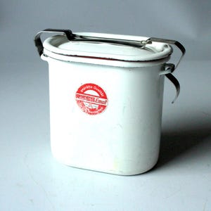 May include: A white rectangular enamel container with rounded corners, featuring a metal locking handle and a red circular sticker on the front that reads RIESS Email, geprufte Qualitat, and Herdarten in white and red text.
