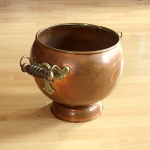 Könnte beinhalten: Ein großer Kupfertopf mit zwei verzierten Griffen und einem runden Boden. Der Topf hat eine gehämmerte Oberfläche und ist aus massivem Kupfer gefertigt.