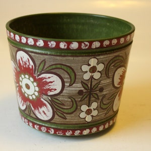 Könnte beinhalten: Ein grüner Keramiktopf mit braunem und weißem Blumenmuster. Der Topf hat einen roten und weißen Rand.