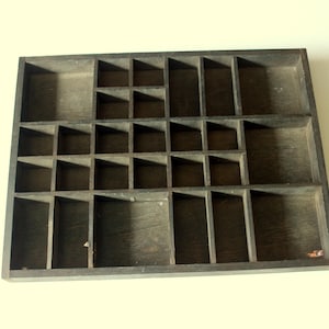 Op de afbeelding: Een donker gebeitste houten displaykist met meerdere kleine compartimenten. De rechthoekige kist heeft een rasterachtig interieur met vierkante en rechthoekige ruimtes van verschillende afmetingen. De houtnerf is zichtbaar en de kist lijkt vintage te zijn.