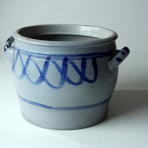 May include: A gray stoneware crock with blue painted designs. The crock has two handles and a rounded body.