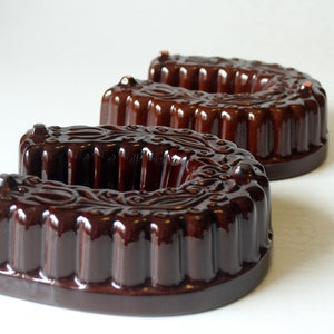 Puede incluir: Dos moldes para pasteles de cerámica marrón con forma de herradura. Los moldes tienen un diseño decorativo y un acabado brillante.