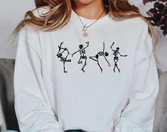May include: White sweatshirt with a graphic of four skeletons in different dance poses. The skeletons are black and the sweatshirt is white.
