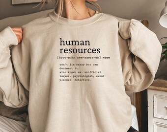 May include: A beige sweatshirt with the text "human resources" and a definition of the term. The definition includes the pronunciation, "[hyoo-muhn ree-sawrs-es]", and describes the role as "can't fix crazy but can document it." It also lists "unofficial lawyer, psychologist, event planner, detective" as other names for the role.