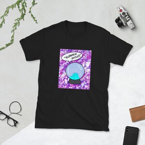May include: Black t-shirt featuring a cartoon graphic of a crystal ball with the text "Nurnheim Sucks!!" in a speech bubble. The crystal ball is set against a purple and white background.