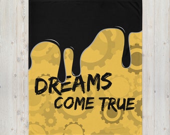 May include: A black and gold throw blanket featuring the text "DREAMS COME TRUE". The top section is black with a dripping design, while the bottom has a gold gear pattern. The blanket is rectangular.