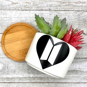 May include: White ceramic planter with a black heart-shaped design featuring the letters "BT" inside. The planter is filled with green and red succulents.