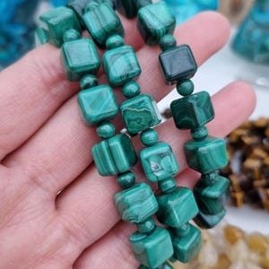 May include: A green malachite bracelet with square beads. The bracelet is made of natural stone and has a unique pattern.