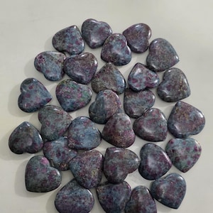 May include: A collection of heart-shaped stones in shades of blue, gray, and burgundy. The polished stones have a marbled appearance, with a mix of colors and textures. The hearts are arranged closely together, creating a visually appealing display.