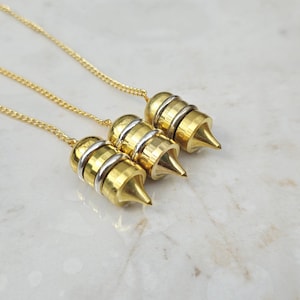 May include: Three gold-toned metal pendulums, each featuring a pointed tip and a silver-toned ring accent, suspended from delicate gold-toned chains. The pendulums have a cylindrical body with a smooth, polished finish and a tapered, conical base.