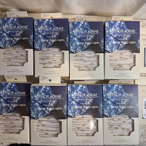 May include: A collection of Manor Lane Shimmer String Lights in boxes, each containing 120 lights and a total length of 20 ft. The boxes have a blue and white design. Also included are LED remote controls.