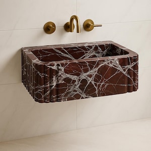 May include: A rectangular, wall-mounted bathroom sink made of red marble with white veining. The sink has a fluted front and is paired with a gold-colored faucet and fixtures. The sink is mounted on a white tiled wall.