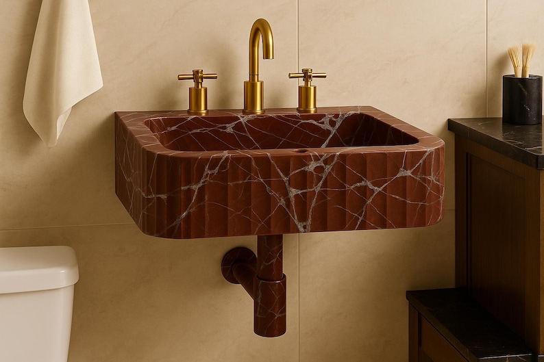 K&ouml;nnte beinhalten: Ein wandmontiertes, rechteckiges Waschbecken aus rotbraunem Marmor mit wei&szlig;en Adern. Das Waschbecken hat eine geriffelte Textur und ist mit goldfarbenen Wasserh&auml;hnen ausgestattet. Ein passendes Abflussrohr erstreckt sich darunter.