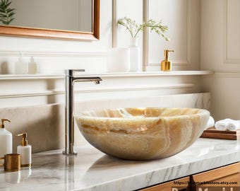 May include: A large, round, natural stone vessel sink in a beige and brown color with a white marble countertop and a chrome faucet.