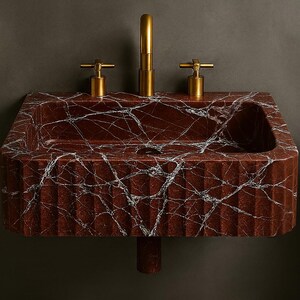 K&ouml;nnte beinhalten: Ein rechteckiges Waschbecken aus rotem Marmor mit wei&szlig;en Adern und einer geriffelten Front. Es hat einen goldenen Wasserhahn und zwei goldene Griffe. Ein Badezimmer-Accessoire. Abmessungen: ca. 70 cm breit.