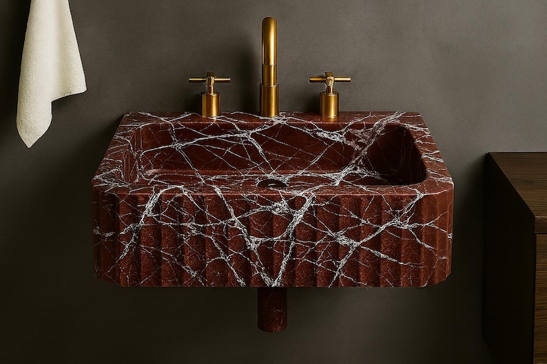 K&ouml;nnte beinhalten: Ein rechteckiges Waschbecken aus rotem Marmor mit wei&szlig;en Adern und einer geriffelten Front. Es hat einen goldenen Wasserhahn und zwei goldene Griffe. Ein Badezimmer-Accessoire. Abmessungen: ca. 70 cm breit.