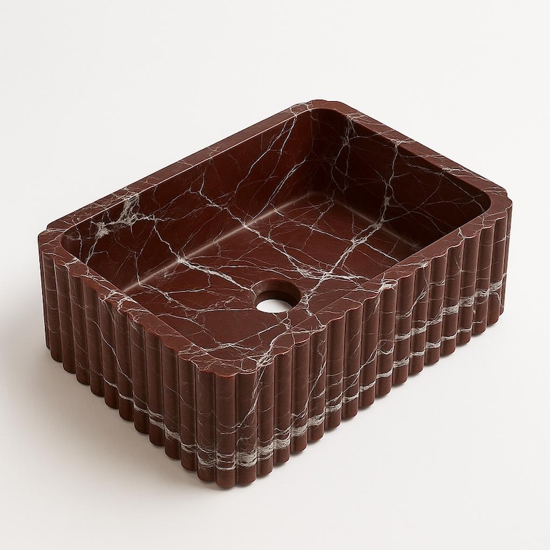 May include: A rectangular, burgundy-colored sink with a fluted exterior and a white marble-like veining pattern. The sink has a single drain hole and is set against a white background. The sink is a bathroom fixture.