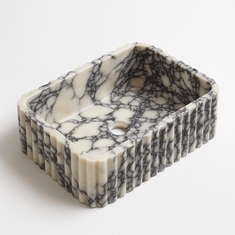 Pu&ograve; includere: Lavandino rettangolare in marmo con un motivo venato bianco e grigio. Il lavandino ha un design esterno scanalato e un foro di scarico circolare. L'estetica generale &egrave; moderna e lussuosa, adatta a un bagno.