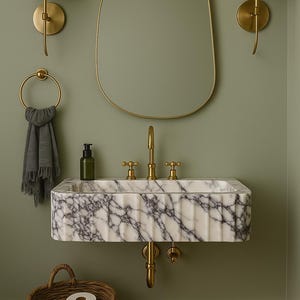Pu&ograve; includere: Un bagno con un lavabo in marmo e rubinetti dorati, uno specchio con cornice dorata e applique a parete. Un cestino in vimini contiene rotoli di carta igienica. Le pareti sono dipinte di un verde tenue, creando un'atmosfera rilassante.