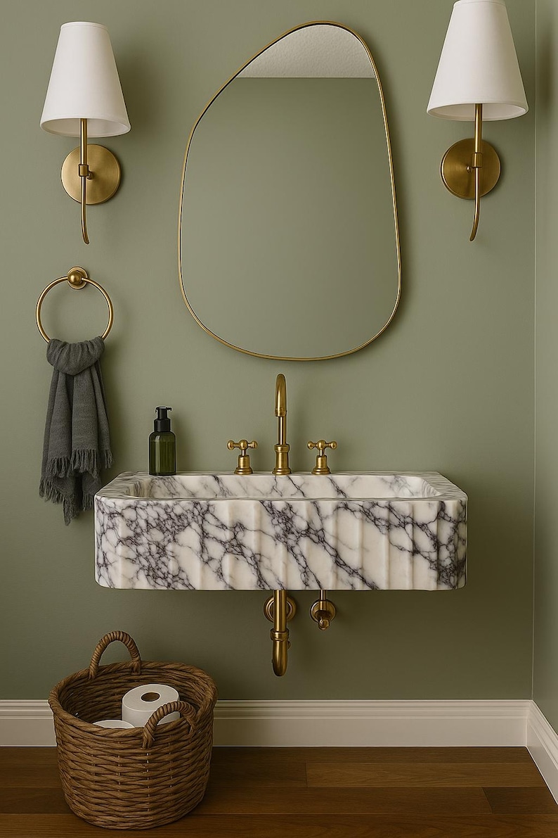 Pu&ograve; includere: Un bagno con un lavabo in marmo e rubinetti dorati, uno specchio con cornice dorata e applique a parete. Un cestino in vimini contiene rotoli di carta igienica. Le pareti sono dipinte di un verde tenue, creando un'atmosfera rilassante.