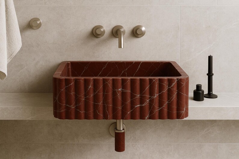 K&ouml;nnte beinhalten: Ein rechteckiges Waschbecken aus rotem Marmor mit geriffeltem Design und wei&szlig;en Adern. Das Waschbecken ist an einer Wand mit einem silbernen Wasserhahn und zwei Kn&ouml;pfen befestigt. Eine schwarze Kerze und eine Flasche stehen auf einem Regal.