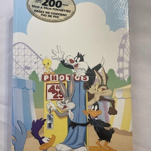 May include: A photo album featuring Looney Tunes characters like Bugs Bunny, Daffy Duck, and Sylvester the Cat. The cover has a light blue background with a roller coaster and carnival tent design. The album holds 200 photos, each 4x6 inches.